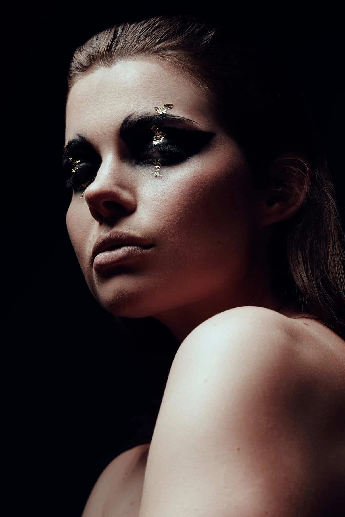 Audrey regard par-dessus l'épaule nue, maquillage noir et strass, fond sombre