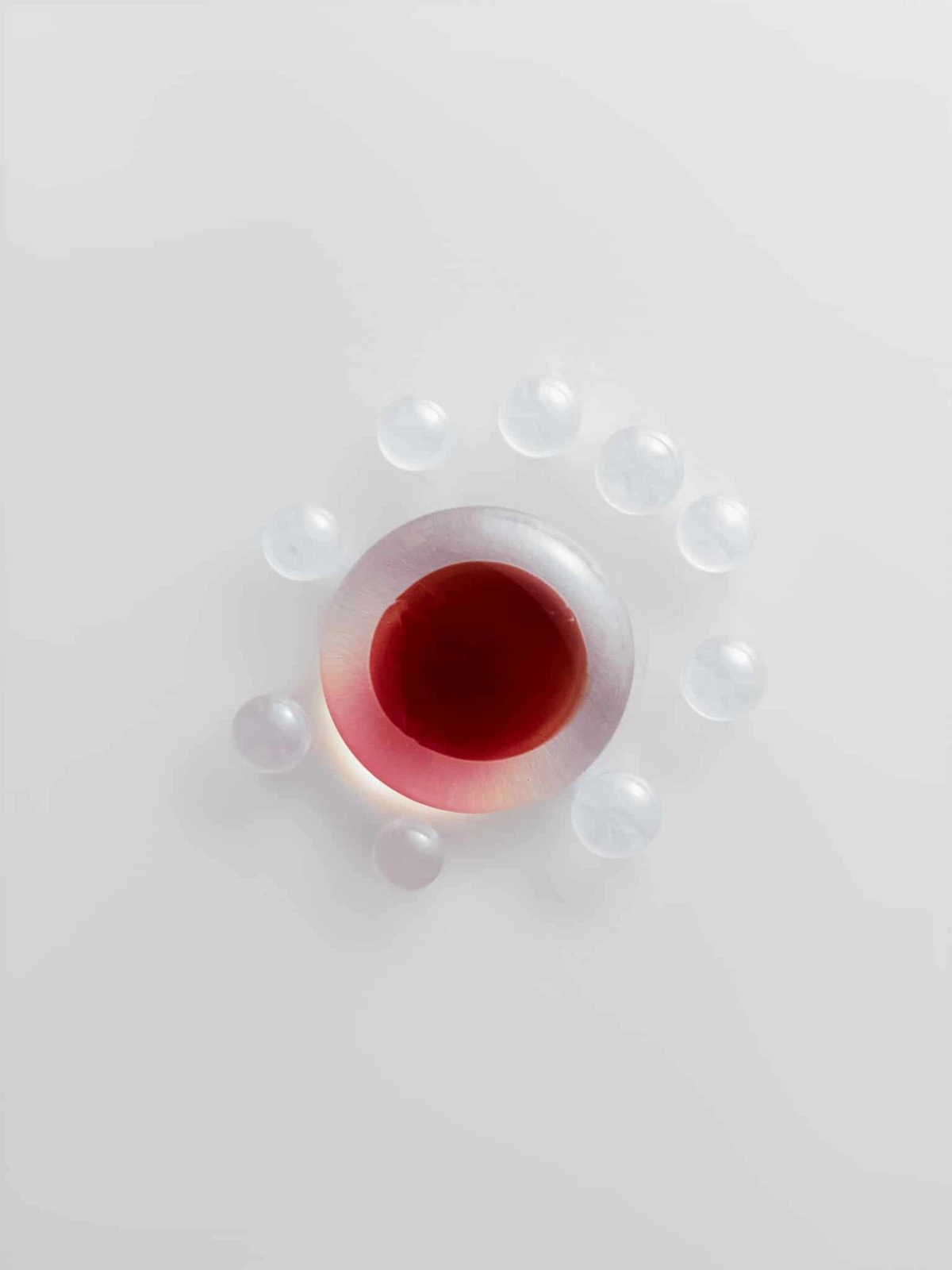 Red drop ringed by small clear bubbles on a white background, macro study of fluids