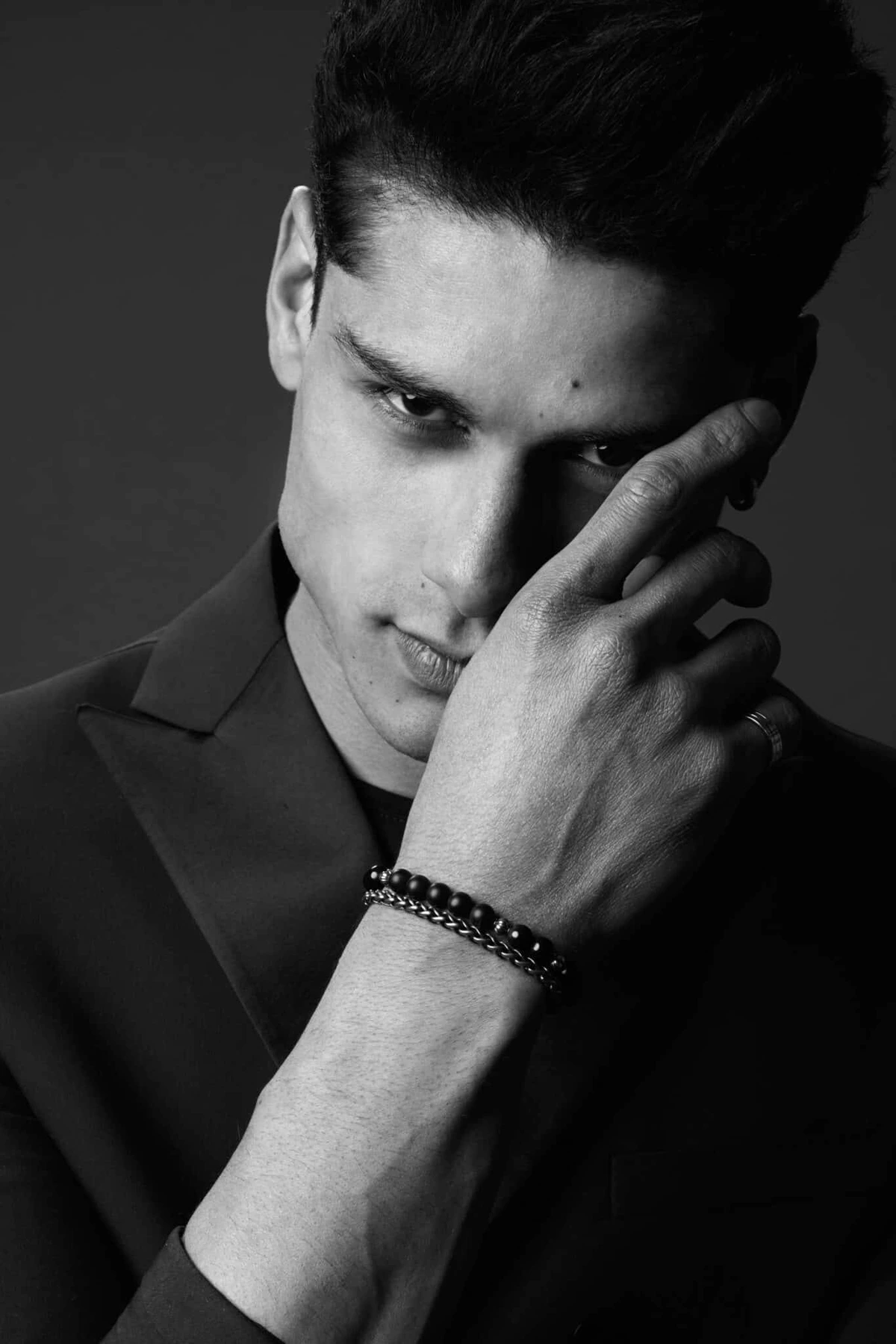Portrait noir et blanc de Hiago, main sur le visage, regard intense, bracelet au poignet