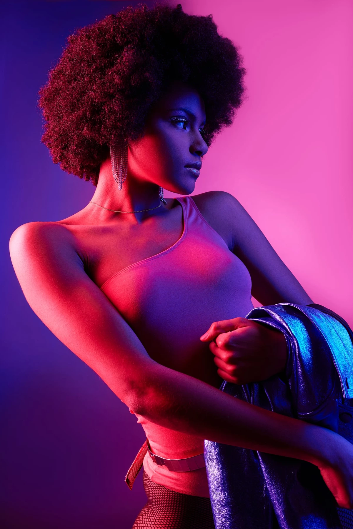 Esmeralda, bras repliés et regard de côté, body rose et veste métallisée, en lumière rose et violette