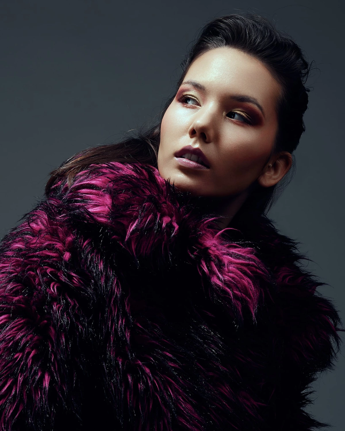 Eliane en manteau de fourrure noire et fuchsia, regard levé sur le côté, fond gris sombre