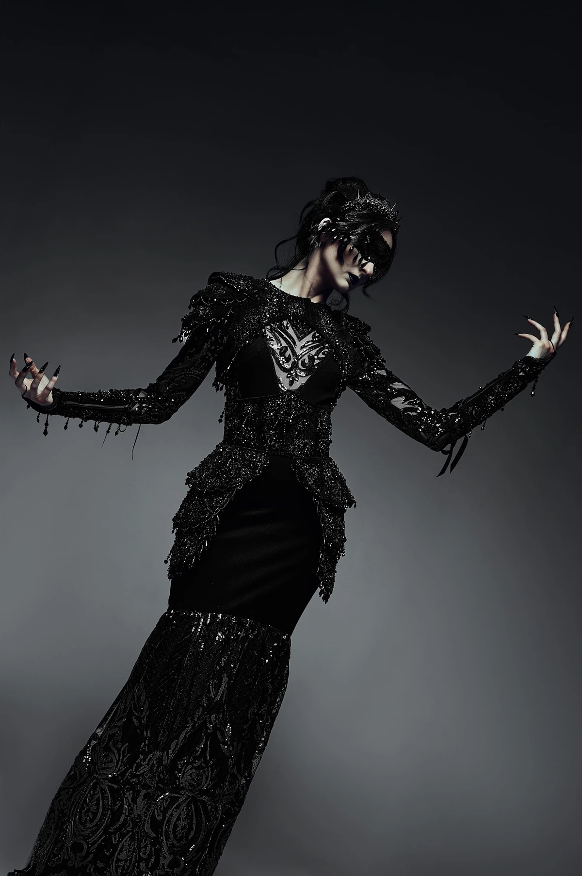 Lucie en princesse sombre, robe noire brodée et masque, bras écartés sur fond gris