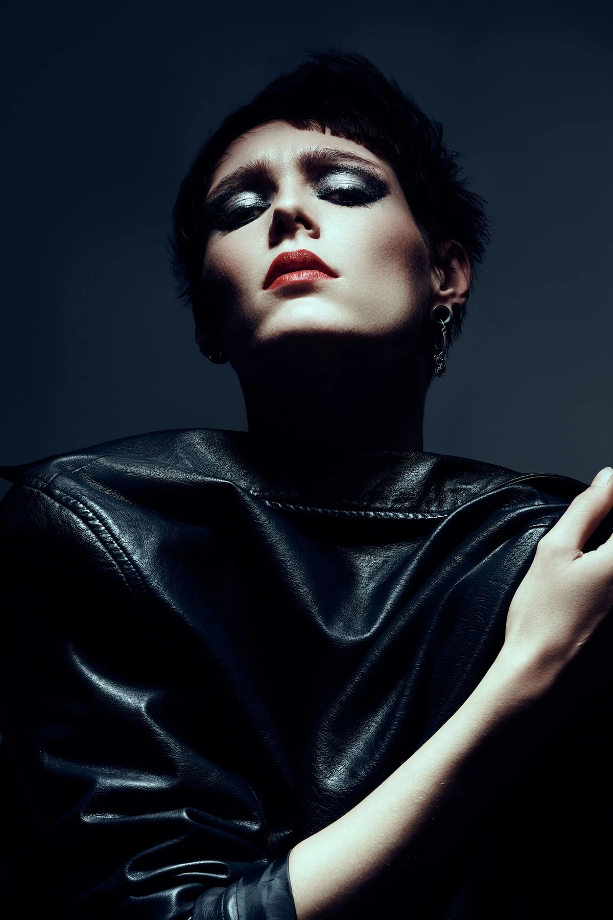Hannah, cheveux courts, yeux mi-clos, veste en cuir noir, lumière dure sur fond bleu nuit