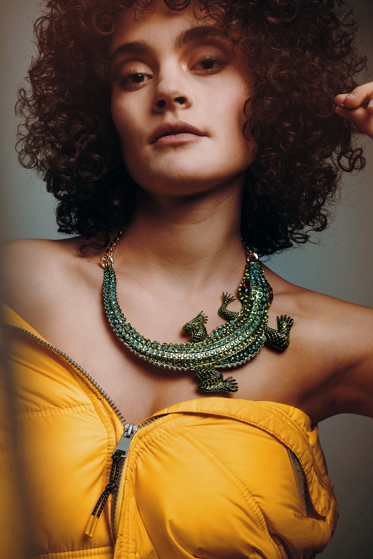 Céline aux cheveux bouclés, collier lézard vert et veste jaune, regard vers l'objectif