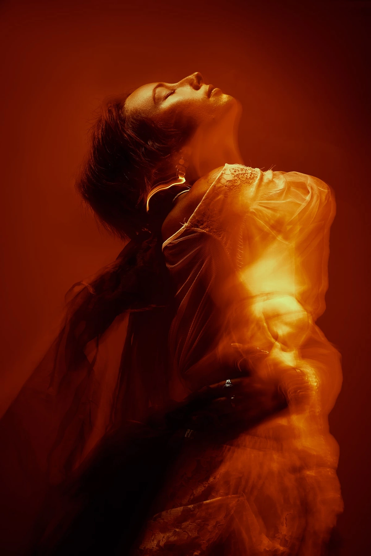 Maeva tête renversée en arrière, vêtements en mouvement dans une lumière orange et rouge