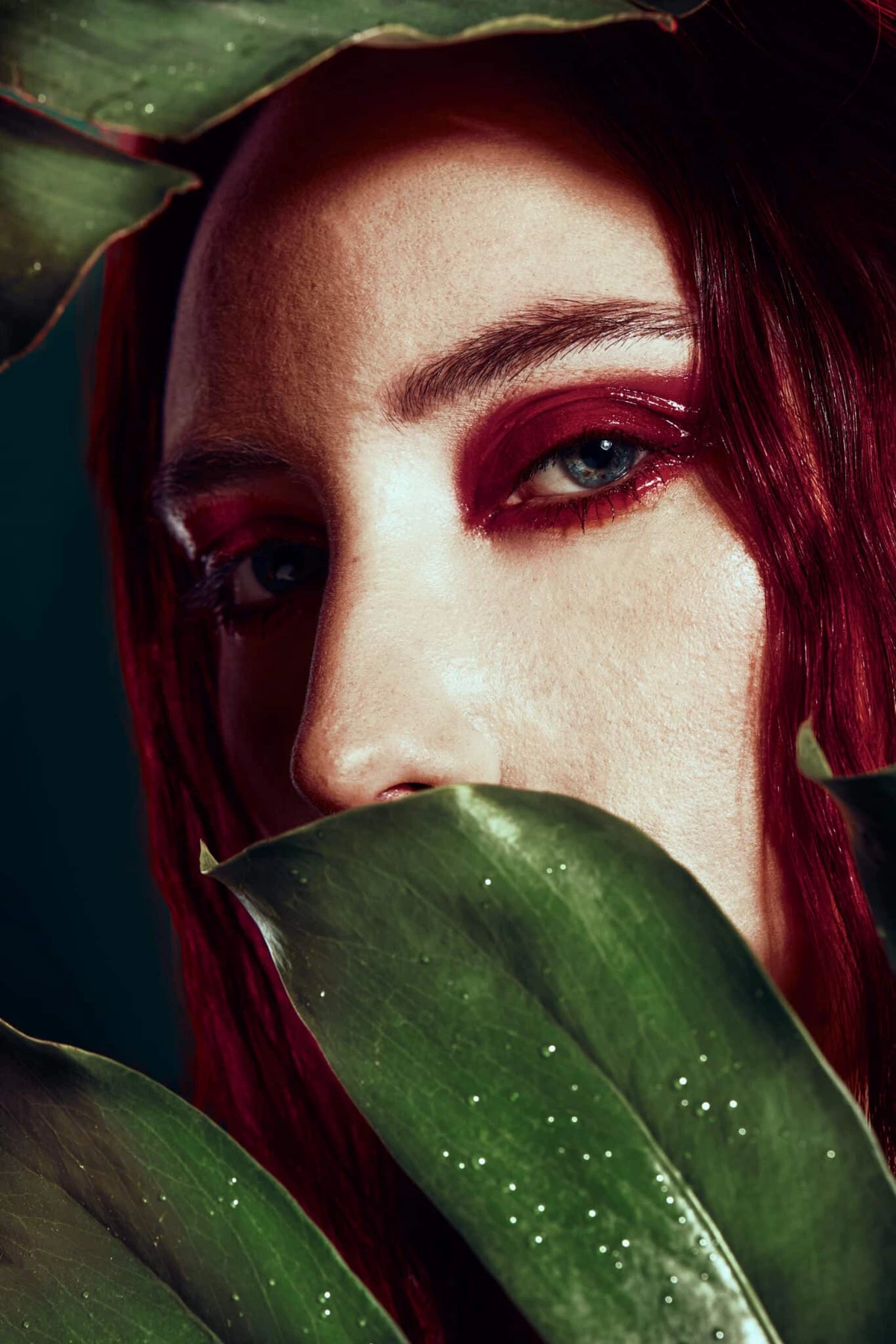 Maeva aux cheveux rouges, maquillage rouge, visage en partie caché par une feuille verte