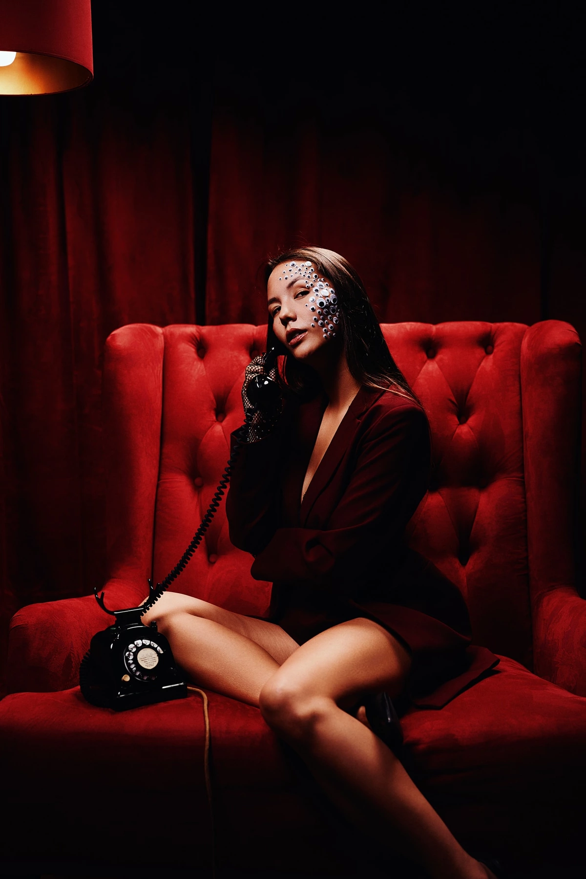 Eliane assise dans un fauteuil capitonné rouge, téléphone ancien à l'oreille, rideaux rouges