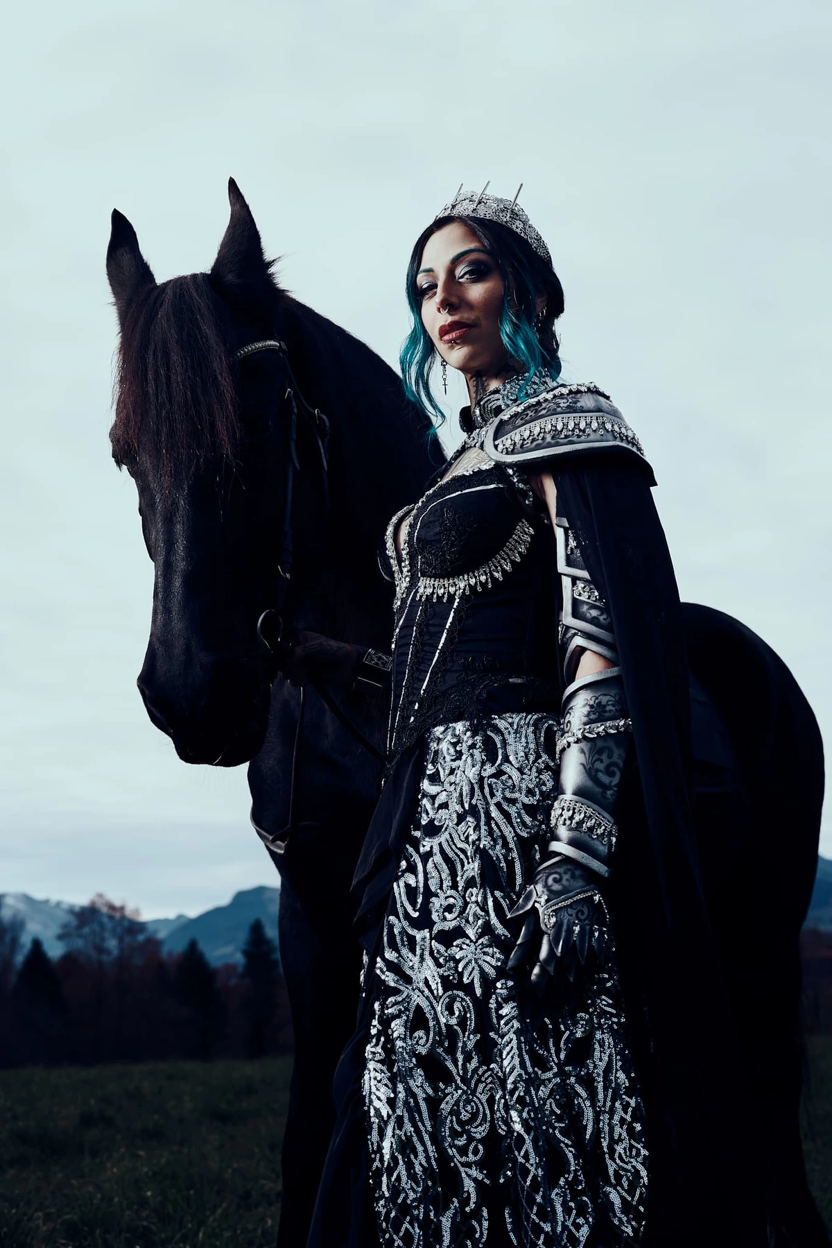 Reine guerrière Twisted Ego en armure brodée et couronne, aux côtés d'un cheval noir, ciel clair