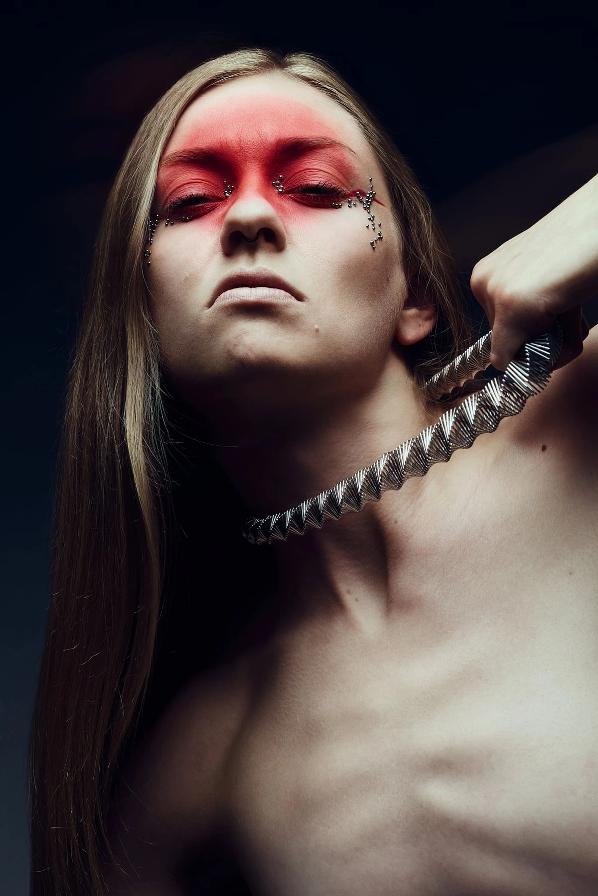 Charlotte Simon, tête levée, tire sur son collier métallique, maquillage rouge graphique sur les yeux