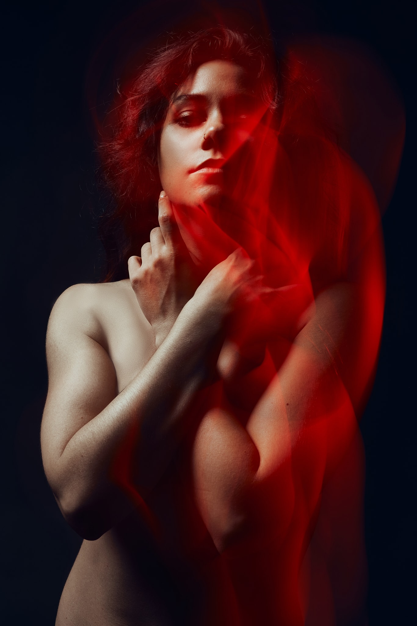 Une personne partiellement nue pose les bras croisés sur la poitrine, baignée dans un éclairage dramatique. Des tourbillons de lumière rouge ou de fumée masquent partiellement son corps sur un fond sombre.