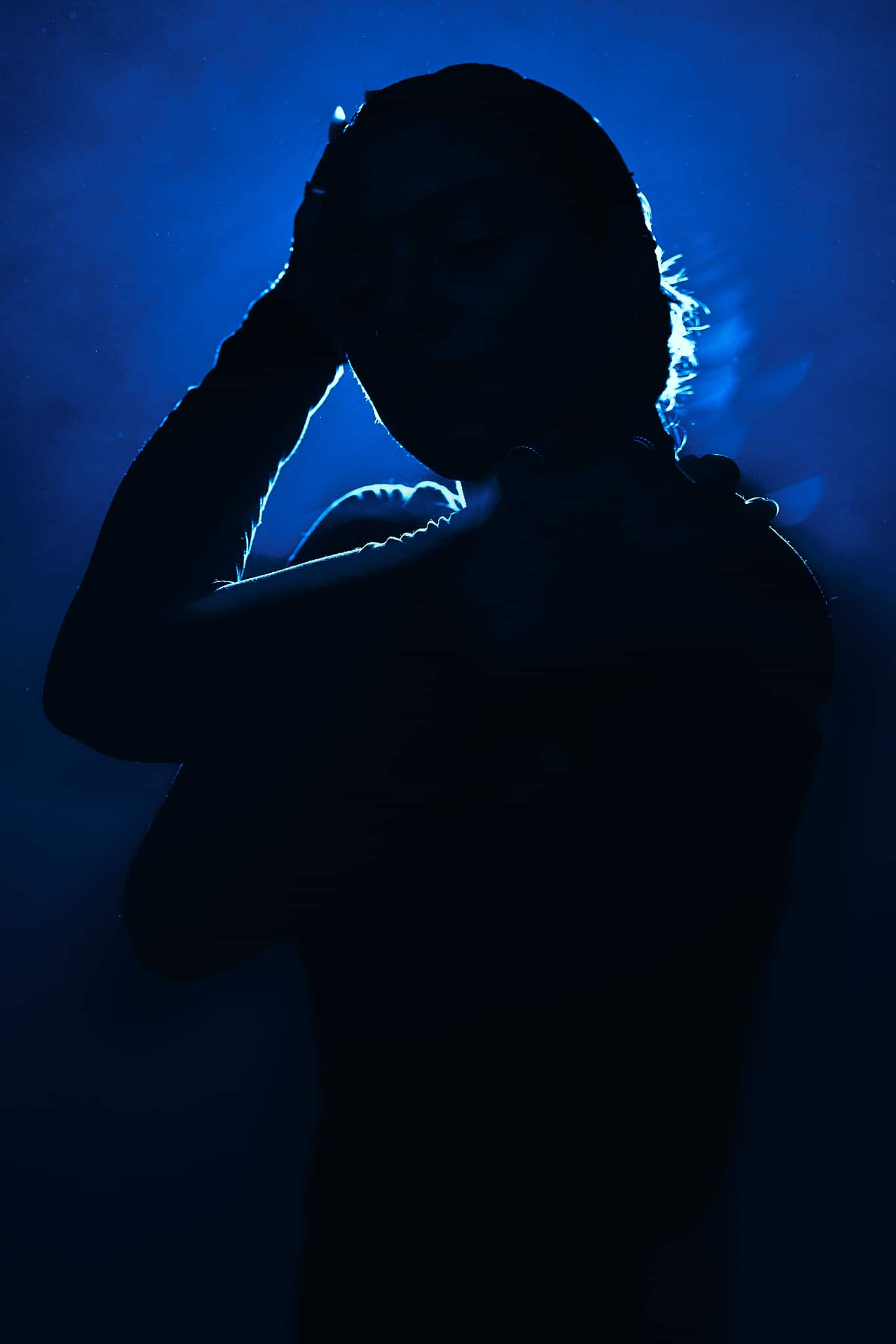 La silhouette d'une personne se détache sur un fond bleu, une main touchant sa tête et l'autre bras sur sa poitrine. Les traits de la personne sont principalement dans l'ombre, ce qui crée un effet dramatique et mystérieux.